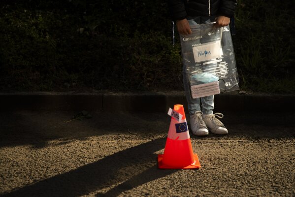 A student holds a bag with a face mask, which reads 'clean', as she waits in a line before entering the classroom at Les Magnolias primary school during the partial lifting of coronavirus, COVID-19, lockdown regulations in Brussels, Monday, May 18, 2020. Belgium is taking the next step in its relaxation of the coronavirus lockdown on Monday, with more students going to school, markets and museums reopening and the snip of a barber's scissors filling the air again. (AP Photo/Francisco Seco)