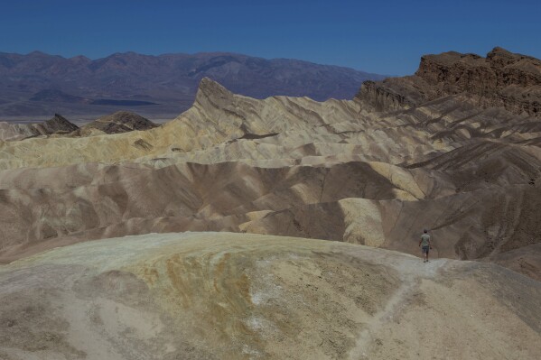 A man walks on a pathway Tuesday, July 11, 2023, in Death Valley National Park, Calif. July is the hottest month at the park with an average high of 116 degrees (46.5 Celsius). (AP Photo/Ty ONeil)