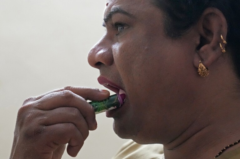 Preethi, a 38-year-old transgender woman who uses only her first name, applies lipstick as she gets ready at home before ferrying passengers in her electric auto rickshaw in Bengaluru, India, Wednesday, July 12, 2023. (AP Photo/Aijaz Rahi)