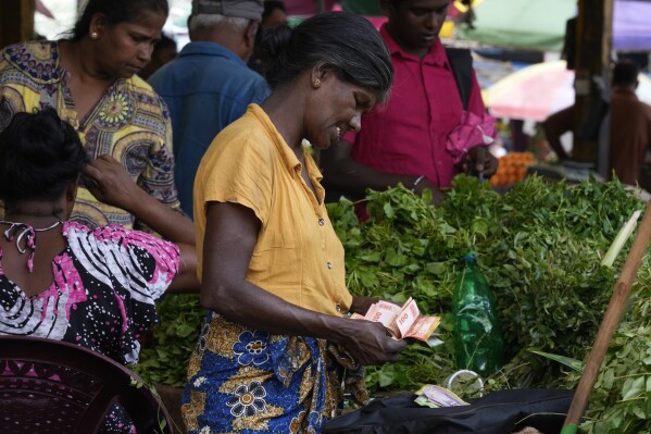 FILE- A vendor counts currency notes as she sells vegetables at a market place in Colombo, Sri Lanka, June. 1, 2023. Sri Lanka has reached an agreement with the Exim Bank of China on key terms and principles for restructuring its debt, a key step toward unlocking a second instalment of a $2.9 billion package from International Monetary Fund aimed at rescuing the island nation from a dire economic crisis. (AP Photo/Eranga Jayawardena, File)