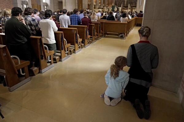 Una mujer y un niño se arrodillan durante la misa católica en el Benedictine College el domingo 29 de octubre de 2023 en Atchison, Kansas (Foto AP/Charlie Riedel).