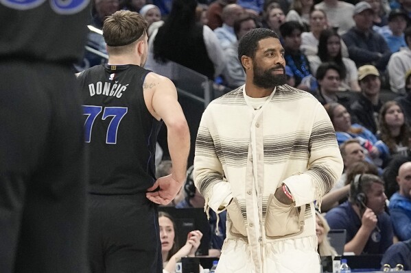 Injured Dallas Mavericks guard Kyrie Irving, right, looks on as teammate Luka Doncic (77) prepares to play during the second half of an NBA basketball game against the Cleveland Cavaliers in Dallas, Wednesday, Dec. 27, 2023. (AP Photo/LM Otero)