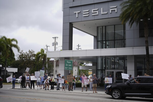 A passing driver signals support to people protesting outside a Tesla dealership as part of a coordinated international day of "Tesla Takedown" protests, Saturday, March 29, 2025, in Miami. (AP Photo/Rebecca Blackwell)