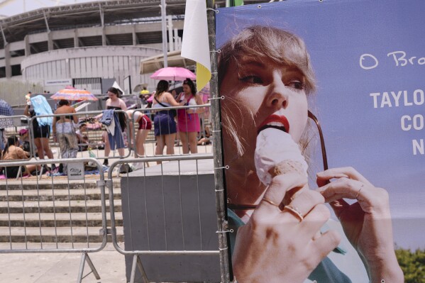 Taylor Swift fans wait for the doors of Nilton Santos Olympic stadium to open for her Eras Tour concert amid a heat wave in Rio de Janeiro, Brazil, Saturday, Nov. 18, 2023. A 23-year-old Taylor Swift fan died at the singer's Eras Tour concert in Rio de Janeiro Friday night, according to a statement from the show's organizers in Brazil. (AP Photo/Silvia Izquierdo)