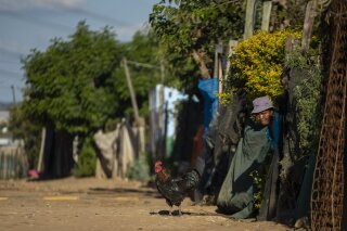 A woman watches as the South African National Defence Forces members patrol the street in Diepsloot informal settlement, north of Johannesburg, South Africa, Thursday, April 16, 2020. South African President Cyril Ramaphosa extended the lockdown by an extra two weeks in a continuing effort to contain the spread of COVID-19 coronavirus. (AP Photo/Themba Hadebe)