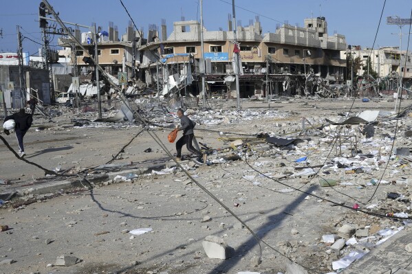 Palestinians walk through destruction by the Israeli bombardment in the Nusseirat refugee camp in Gaza Strip, Tuesday, Jan. 16, 2024. (AP Photo/Adel Hana)