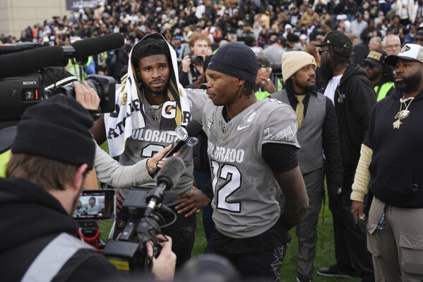 Colorado wide receiver Travis Hunter, right, answers a question as quarterback Shedeur Sanders looks on as the pair are interviewed following an NCAA college football game against Utah, Saturday, Nov. 16, 2024, in Boulder, Colo. (AP Photo/David Zalubowski)