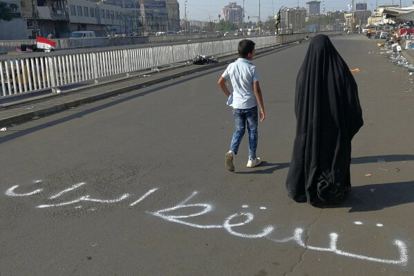 People walk by an Arabic sentence writing on the asphalt reads "Down with Iran" near the site of the protests at Tahrir Square during anti-government ongoing protests in Baghdad, Iraq, Friday, Nov. 1, 2019. (AP Photo/Khalid Mohammed)