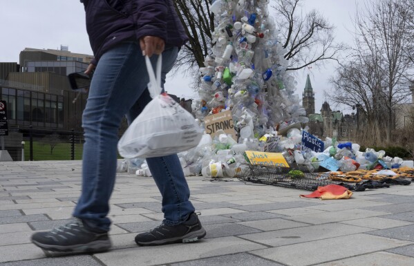 ARCHIVO - Una persona sostiene comida en una bolsa de plástico frente a una instalación de arte afuera de la Conferencia de las Naciones Unidas sobre Plásticos el 23 de abril de 2024, en Ottawa, Ontario.  (Adrian Wild/The Canadian Press vía AP, archivo)
