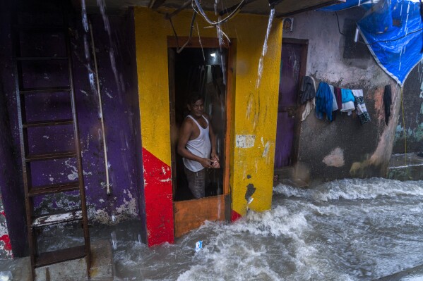 An Indian man stands at the door of his house as waves caused by high tide hits the huts on the shore of the Arabian Sea in Mumbai, India, Thursday, July 6, 2023. (AP Photo/Rafiq Maqbool)