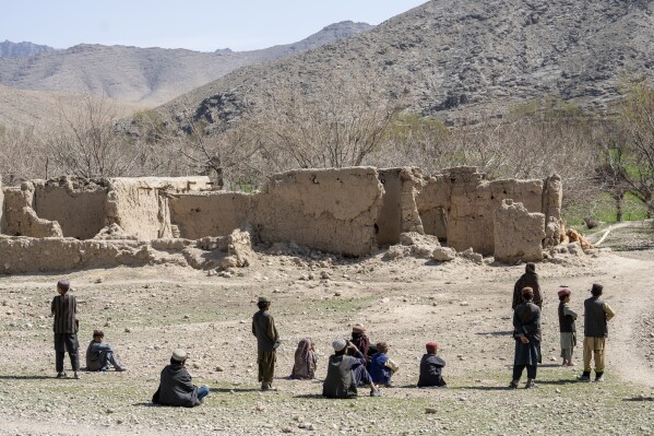 Children stand in front of a home destroyed during a Sept. 5, 2019, night raid by U.S. forces in a village in a remote region of Afghanistan, on Friday, Feb. 24, 2023. The windowless one-story compound was made of mud and straw. Like many in this conservative region, women stayed within the walls for most of their lives. (AP Photo/Ebrahim Noroozi)