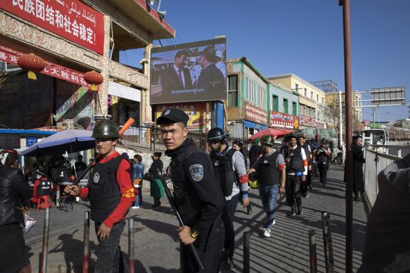 FILE - Armed civilians patrol the area outside the Hotan Bazaar where a screen shows Chinese President Xi Jinping in Hotan in western China's Xinjiang region, Nov. 3, 2017. China's discriminatory detention of Uyghurs and other mostly Muslim ethnic groups in the western region of Xinjiang may constitute crimes against humanity, the U.N. human rights office said in a long-awaited report Wednesday, Aug. 31, 2022, which cited "serious" rights violations and patterns of torture in recent years. (AP Photo/Ng Han Guan, File)