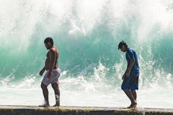 People walk in front of the high surf near Kapahulu Groin (Waikiki Wall) in Waikiki, Hawaii, Sunday, July 17, 2022. (Craig T. Kojima/Honolulu Star-Advertiser via AP)