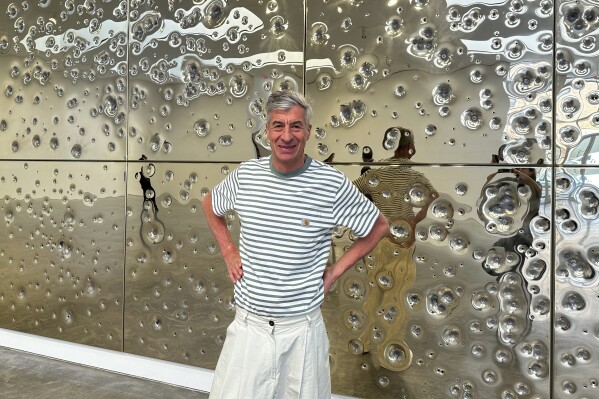 Italian artist Maurizio Cattelan poses with his installation, "Sunday," at Gagosian gallery on May 1, 2024, in New York. The installation consists of 64 panels plated with 24-karat gold and pockmarked by gunfire. (AP Photo/Jocelyn Noveck)