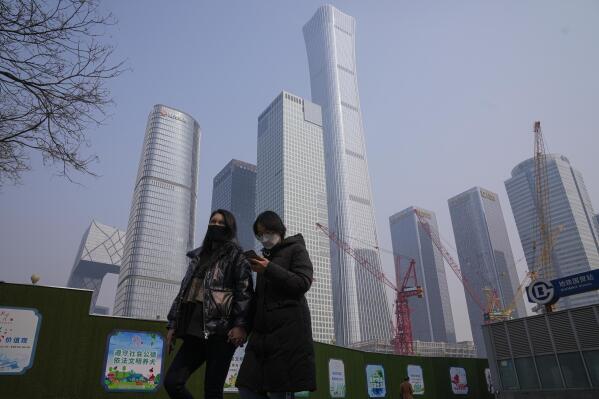 Women wearing face masks walk by government's propaganda posters near the construction cranes at the central business district in Beijing on Feb. 27, 2023. Chinese economic officials expressed confidence Monday, March 6, 2023 they can meet this year’s growth target of "around 5%" by generating 12 million new jobs and encouraging consumer spending following the end of anti-virus controls that kept millions of people at home. (AP Photo/Andy Wong)