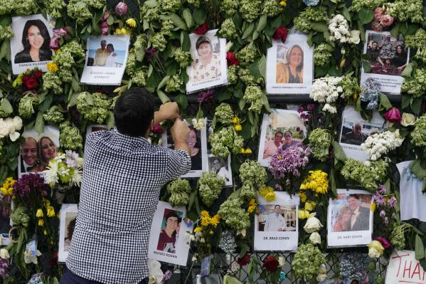 Leo Soto, whose high school friend Nicole Langesfeld is missing, along with her husband Luis Sadovnic, adjusts pictures at the makeshift memorial he began to the scores of people who were left missing after the Champlain Towers South condo building partially collapsed nearly a week ago, Wednesday, June 30, 2021, in Surfside, Fla.. (AP Photo/Gerald Herbert)