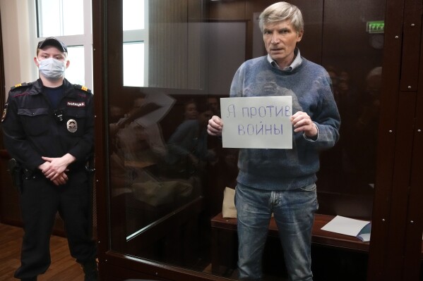 FILE - Alexei Gorinov holds a sign "I am against the war" standing in a cage during hearing in the courtroom in Moscow, Russia, Tuesday, June 21, 2022. (AP Photo, File)