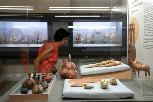 A woman passes behind antiquities repatriated from Germany and put on display at the Archeological museum, in capital Nicosia, Cyprus, Monday, July 22, 2024. The returned artifacts numbering around 60, including jewelry from the Chalcolithic Period dating between 3500-1500 BC, Bronze Age bird-shaped idols, jars and spearheads as well as many Orthodox Christian icons were part of a larger haul of 250 antiquities that German authorities had seized from Turkish art dealer Aydin Dikmen in 1997. (ĢӰԺ Photo/Petros Karadjias)