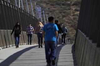 Unas personas caminan en un puente en el Puerto de Entrada de San Ysidro, que conecta la ciudad mexicana de Tijuana con Estados Unidos, el miércoles 13 de octubre de 2021, en San Diego. (AP Foto/Gregory Bull)