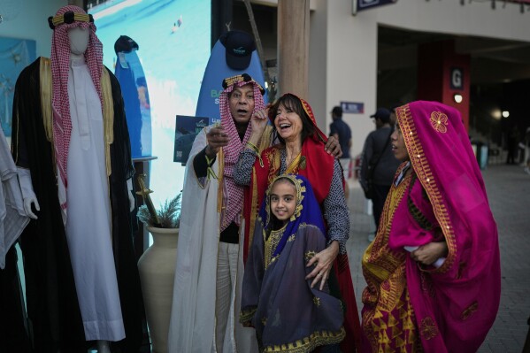 F1 fans react after trying on traditional local dresses at the Formula One Bahrain Grand Prix Village at the Bahrain International Circuit in Sakhir, Bahrain, Saturday, April 12, 2025. (AP Photo/Altaf Qadri)