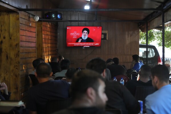 People watch the speech of Hezbollah leader Hassan Nasrallah on a tv screen as they sit in a cafe in the southern suburbs of Beirut, Thursday, Sept. 19, 2024. (AP Photo/Hassan Ammar)