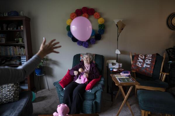 Betty Bednarowski, 79, smiles as she bats a balloon back and forth with a nursing assistant at home, Tuesday, Nov. 30, 2021, in Rotterdam Junction, N.Y. It's been a year since her family took her out of a nursing home locked down against COVID-19 to rescue her from isolation and neglect. (AP Photo/Wong Maye-E)