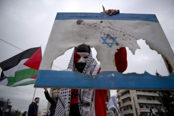 A man holds a burned Israeli flag, during a protest in front of the Israeli Embassy in Athens, Greece, Saturday, Jan. 27, 2024. Around 3,000 people staged a protest march early Saturday afternoon against the continuing Israeli military operations in Gaza. (AP Photo/Michael Varaklas)