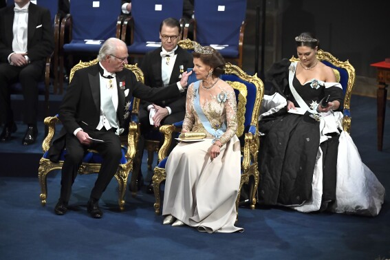 FILE - Sweden's King Carl Gustaf adjusts a pillow for Queen Silvia at the Nobel award ceremony at Stockholm Concert Hall, in Stockholm, on Tuesday Dec. 10, 2019. (Claudio Bresciani / TT Pool via AP, File)