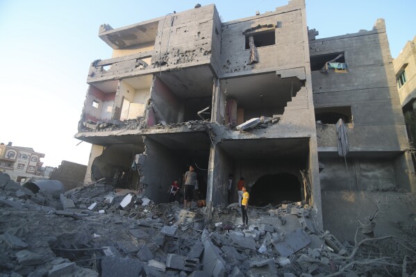 Palestinians stand by a building destroyed in an Israeli airstrike in the Rafah border, Gaza Strip, on Monday, Oct. 16, 2023. (AP Photo/Hatem Ali)