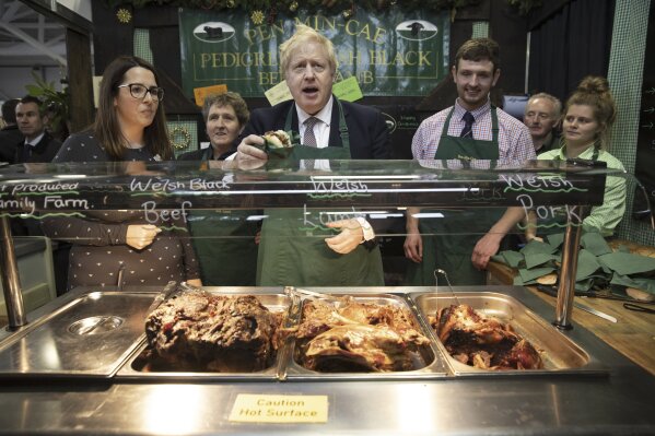 Britain's Prime Minister Boris Johnson greets customers on a stall selling meat sandwiches at the Welsh County Show in Llanelwedd, Wales, Monday Nov. 25, 2019. Boris Johnson’s party is campaigning heavily on a promise to “get Brexit done” by taking Britain out of the European Union on the scheduled date of Jan. 31, if it wins the election. (Dan Kitwood/Pool via AP)