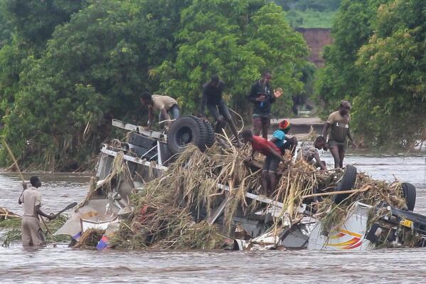In this image made from video, people stand on an overturned vehicle swept by flooding waters in Chikwawa, Malawi, Tuesday Jan. 25, 2022. Mozambique, Madagascar and Malawi are counting the deaths and damage by tropical storm Ana and more than a week of heavy rains across southern Africa. (AP Photo)