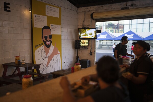 Patrons sit at a food store decorated with a mural of El Salvador President Nayib Bukele, who is running for re-election, in downtown San Salvador, El Salvador, Monday, Jan. 29, 2024. (AP Photo/Moises Castillo)