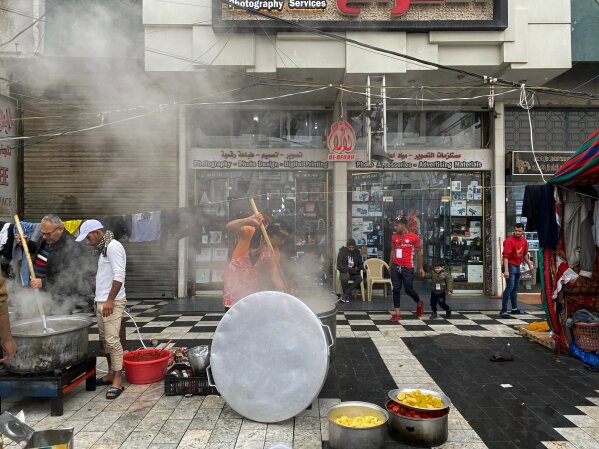 In this Sunday, Dec. 15, 2019 photo, anti-government protesters cook food in front of empty and closed shops in Tahrir square, Baghdad, Iraq.  With Iraq's leaderless uprising now in its third month, the protracted street hostilities, internet outages, blocked roads and a general atmosphere of unease are posing risks to Iraq's economy. In particular, the unrest has set back the most fragile segment of the country's economy, the private sector, where business owners have faced losses from damage to merchandise and disruptions of markets and from consumers reeling in their spending out of fear for the future. (AP Photo/Khalid Mohammed)