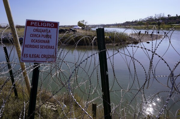 Migrants cross the Rio Grande into the U.S. from Mexico behind Concertina wire and a sign warning that it's dangerous and illegal to cross, Wednesday, Jan. 3, 2024, in Eagle Pass, Texas. According to U.S. officials, a Mexican enforcement surge has contributed to a sharp drop in illegal entries to the U.S. in recent weeks. (AP Photo/Eric Gay)