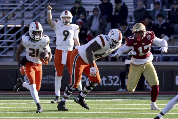 Miami quarterback Tyler Van Dyke (9) signals as Miami running back Henry Parish Jr. (21) runs the ball during the second half of an NCAA college football game against Boston College on Friday, Nov. 24, 2023, in Boston.  (AP Photo/Mark Stockwell)