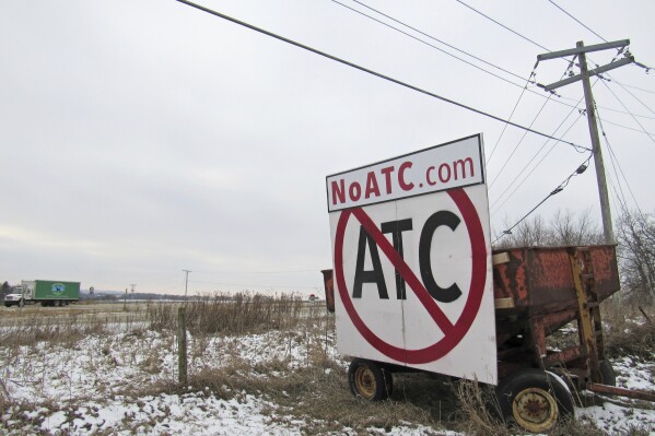 FILE - A grain wagon supports a sign against the proposed transmission line by American Transmission Company, ITC Midwest and Dairyland Power Cooperative, along Highway 18-151 near Ridgeway, Wis., Dec. 8, 2018. Utilities looking to finish building a high-voltage power line linking Iowa and Wisconsin completed a contentious land deal Thursday that allows them to build on a Mississippi River federal wildlife refuge. (Barry Adams/Wisconsin State Journal via AP, File, File)