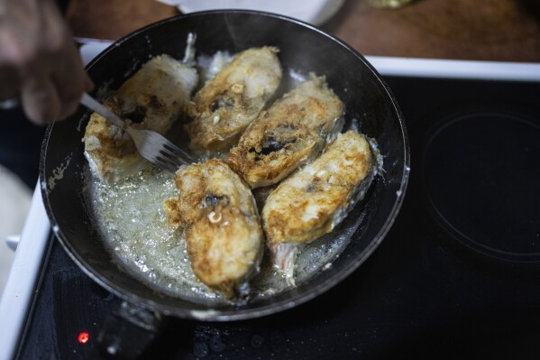 Natalia Zhyvohliad, an internally displaced person from Nova Petrivka in the Zaporizhzhia region of Ukraine, fries fish for her children at the IDP shelter in Kyiv, on Friday, Jan. 19, 2024. (AP Photo/Evgeniy Maloletka)