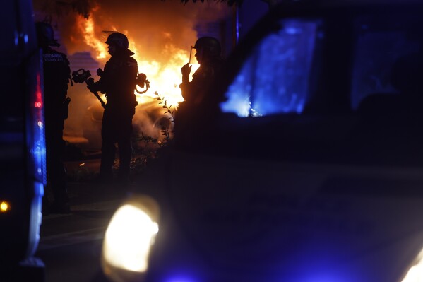 Riot police stand near a burning car in the La Meinau neighborhood of Strasbourg, eastern France, on Friday, June 30, 2023. Young rioters clashed with police and looted stores Friday in a fourth day of violence triggered by the deadly police shooting of a teen, piling more pressure on President Emmanuel Macron after he appealed to parents to keep children off the streets and blamed social media for fueling unrest. (AP Photo/Jean-Francois Badias)