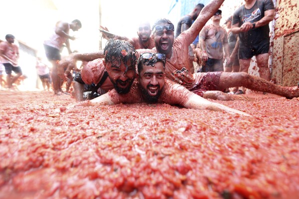 People react during the annual tomato fight fiesta called" Tomatina" in the village of Bunol near Valencia, Spain, Wednesday, Aug. 30, 2023. Thousands gather in this eastern Spanish town for the annual street tomato battle that leaves the streets and participants drenched in red pulp from 120,000 kilos of tomatoes. (AP Photo/Alberto Saiz)