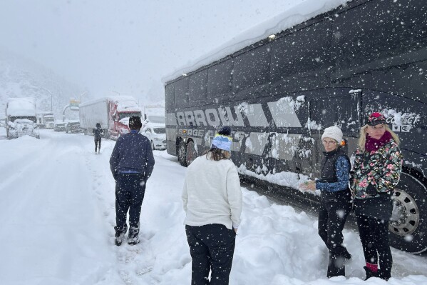 In this photo provided by Bette Davis, people stand outside stranded vehicles on Interstate 70 in Colorado, including a ski bus, on Wednesday, March 13, 2024. A weekly ski trip for about 50 women from the Denver area turned into an overnight ordeal when their bus got stuck in a snowstorm behind jackknifed semi tractor-trailers on their way back from Vail. (Bette Davis via AP)