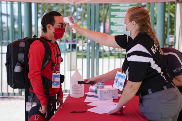 Ricardo Zapata, left, a photographer for the Los Angeles Angels, has his temperature taken by Sarah Morris before entering Angels Stadium for baseball practice on Monday, July 6, 2020, in Anaheim, Calif. New protocols like temperature checks, social distancing, and limiting amount of people allowed in sports venues have been put in place due to the spread of COVID-19. (AP Photo/Ashley Landis)