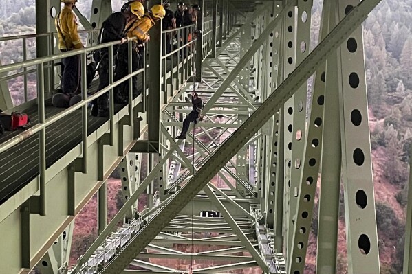 This photo provided by The Placer County Sheriff's Office shows deputies responding to a 19-year-old who was rescued after a social media stunt went wrong and left the teen dangling by a rope from a bridge over the North Fork American River in Placer County, California's tallest bridge. Deputies responding Monday, Sept. 18, 2023, to the Foresthill Bridge determined the teen and his 17-year-old friend had been filming him swinging from the steel span, the Placer County Sheriff's Office said. (The Placer County Sheriff's Office via AP)