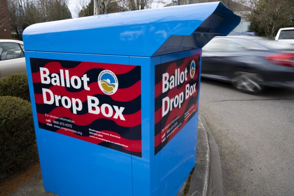 A car drives by a ballot drop box on Wednesday, March 6, 2024, in Sherwood, Ore. In Oregon's Multnomah County, home to Portland, the progressive district attorney who took office during the historical social justice movement of 2020 is being challenged by a more centrist candidate vowing to be tough on crime, highlighting the growing pressure on liberal prosecutors across the U.S. amid voter concerns over public drug use and disorder. (AP Photo/Jenny Kane)