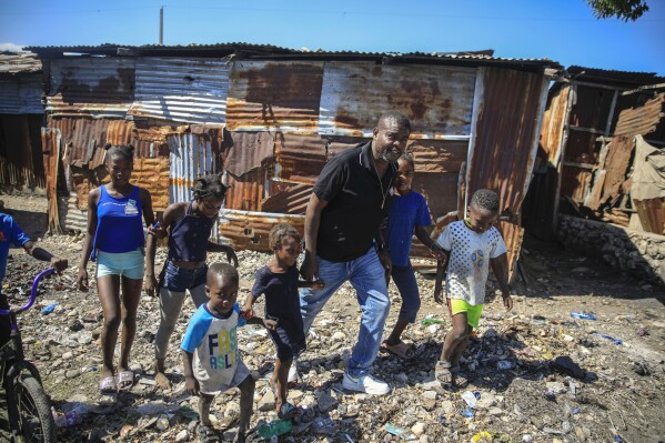 FILE - Jimmy Cherizier, a former elite police officer known as Barbecue who now runs a gang federation, walks hand in hand with children as he visits La Saline district of Port-au-Prince, Haiti, Jan. 24, 2023. Internationally, Cherizier is known as Haiti's most powerful and feared gang leader, sanctioned by the United Nations for "serious human rights abuses," and the man behind a fuel blockade that brought the Caribbean nation to its knees in late 2022. (AP Photo/Odelyn Joseph, File)