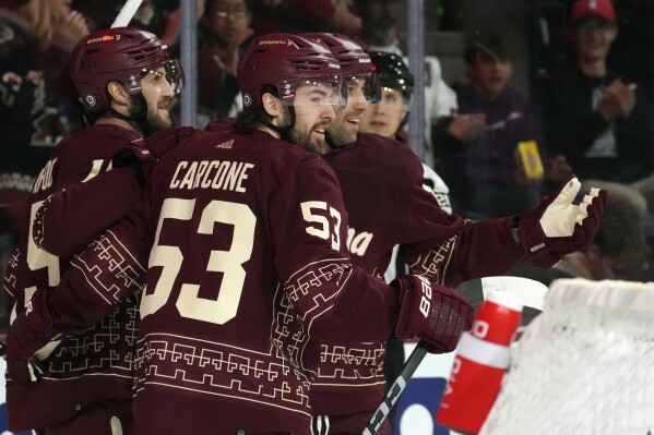 Arizona Coyotes left wing Michael Carcone (53) smiles as he celebrates his goal against the St. Louis Blues with Coyotes left wing Jason Zucker, right, and Coyotes center Alexander Kerfoot, left, during the first period of an NHL hockey game Saturday, Dec. 2, 2023, in Tempe, Ariz. (AP Photo/Ross D. Franklin)