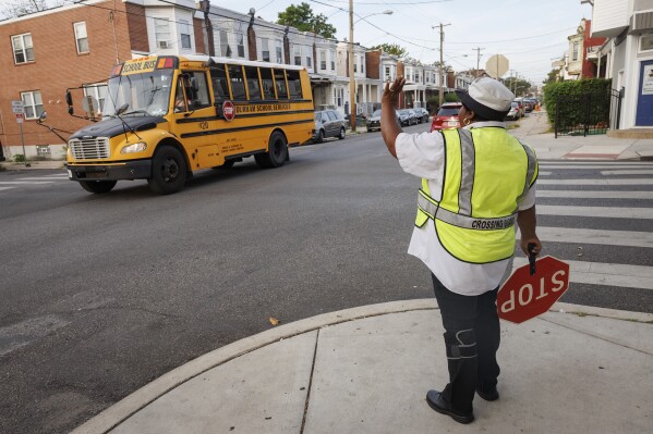 Crossing guard Pamela Lane waves a school bus passing her intersection, Master and N. 57th Street as she crosses students going to Bluford Elementary School, Tuesday, Sept. 5, 2023, in Philadelphia. Today is the first day of school of Philadelphia public school students on Tuesday. (Alejandro A. Alvarez/The Philadelphia Inquirer via AP)