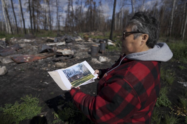 Julia Cardinal, right, shows a photo of what her cabin looked like before it was destroyed by wildfires, near Fort Chipewyan, Canada, on Sunday, Sep. 3, 2023. (AP Photo/Victor R. Caivano)