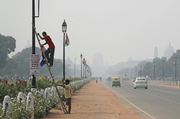 India's Presidential Palace, in the backdrop, is covered with smog as a municipal worker removes flags from a light pole along Rajapth, the ceremonial boulevard in New Delhi, India, Wednesday, Oct. 16, 2019. The Indian capital's air quality levels have plunged to "poor," a day after the government initiated stricter measures to fight chronic air pollution. The state-run Central Pollution Control Board's air quality index for New Delhi stood at 299 on Wednesday, about six times the recommended level. (AP Photo/Altaf Qadri)