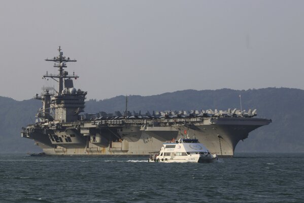 
              FILE - In this March 5, 2018, file photo, a Vietnamese passenger boat sails past U.S. aircraft carrier USS Carl Vinson as it docks in Danang bay, Vietnam. A U.S. sailor has pleaded g...