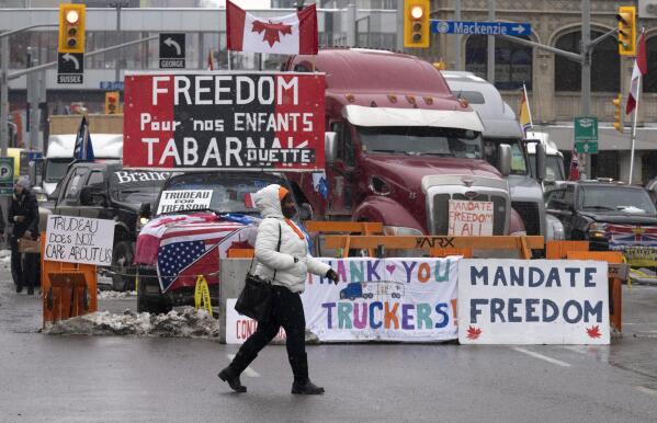 A woman crosses the street in front of vehicles parked as part of the trucker protest,  Tuesday, Feb. 8, 2022 in Ottawa.  Canadian lawmakers expressed increasing worry about protests over vaccine mandates other other COVID restrictions  after the busiest border crossing between the U.S. and Canada became partially blocked.   (Adrian Wyld /The Canadian Press via AP)
